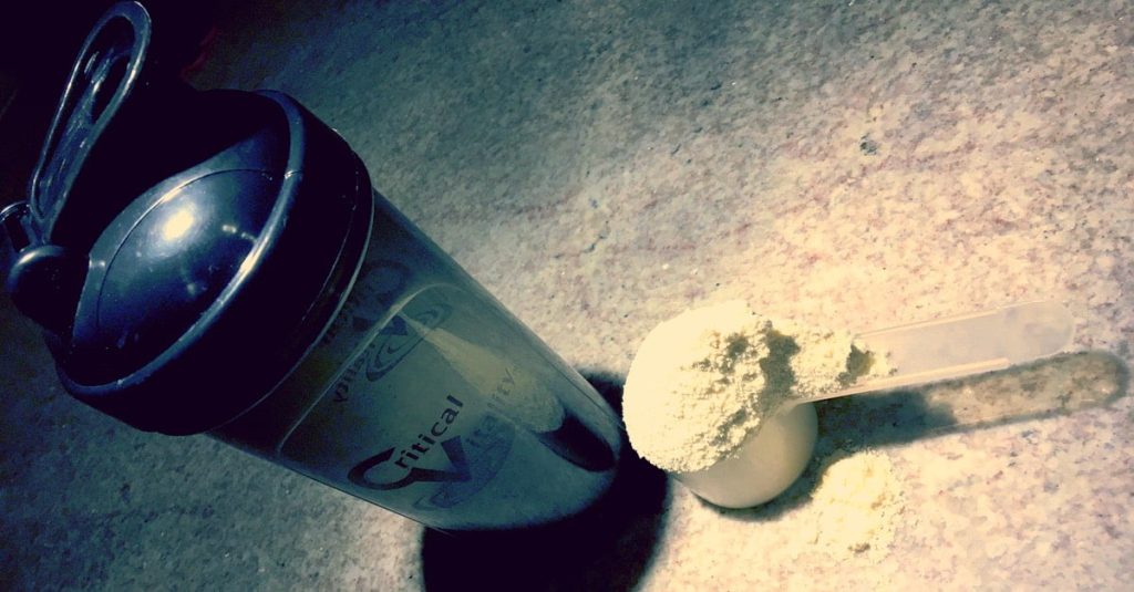 Protein Shaker bottle next to a scoop of protein power. To remind you to Drink Protein Shakes.